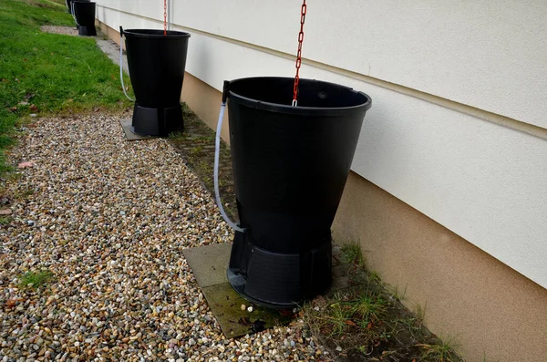 stock image use of a rain roof at new school building. overflow from roof flows down pipe into a barrel with a hose to fill watering can in vegetable garden. pebble border around building, facade, plaster wall