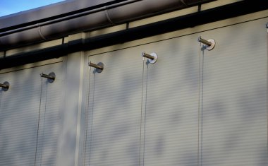 The sheet metal wall of the warehouse is improved with stainless steel cable holders for climbing plants. trellises made of stainless steel vertical cables. in a narrow strip of flowerbed covered 
