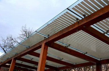 terrace with wooden pergola and plexiglass roof. vines are straining, crawling under the beams. garden or park. sitting with dry wall wine region. restaurant countryside france, truss