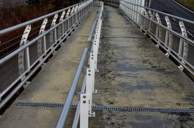 the pedestrian bridge is a long sloping ramp with a stainless steel railing dividing the part for wheelchair users and pedestrians. if the wheelchair user could no longer climb hill, handrail hold on 