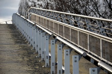 the pedestrian bridge is a long sloping ramp with a stainless steel railing dividing the part for wheelchair users and pedestrians. if the wheelchair user could no longer climb hill, handrail hold on 