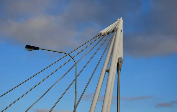 metal rod with pins for fixing the body of the bridge. a white steel pillar on which several gray struts are anchored in a fan-like fashion. roadway suspension bridge structure