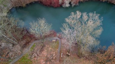 by the lake with green water there is a viewing pier made of terrace boards on the shore. around a pond similar to the lakes in Croatia. deciduous trees around the coast, green, red, blue, upper view