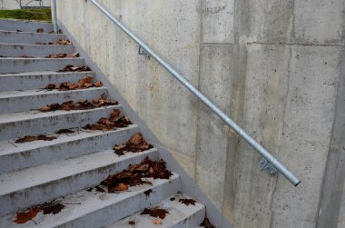 concrete wall made of cast concrete for formwork. the galvanized handle is attached to the wall. the staircase is covered in autumn leaves. gray, cement