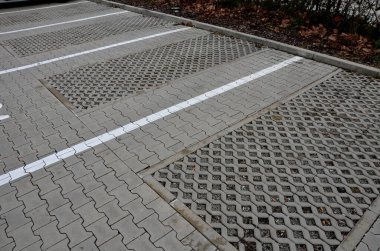 new infiltration parking lot made of porous concrete tiles in a regular square grid with holes filled with gravel. in connection with the asphalt road and the sidewalk with interlocking paving