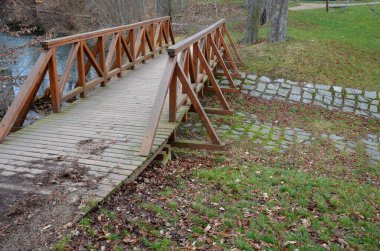 pedestrian bridge over a small gorge and a stream. it consists of two steel crossbeams. as the surface and railing of the bridge is made of brown painted planks. is long and narrow. polder wild