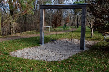 Massive wood beams in the shape of a square gate or frame, between which is a metal rod on which are swings for children. lawn by the park path. roof, metal sheet, aerial, view  footpath, lawn