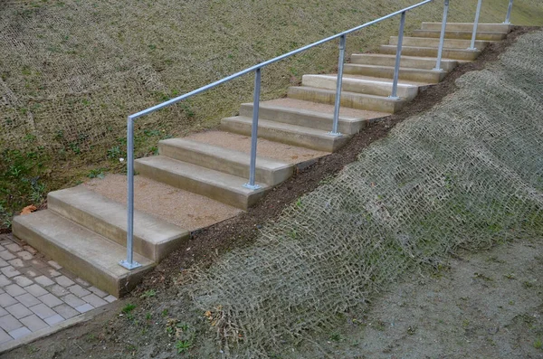 outdoor park stairs on a slope. jute mat protects against erosion. seed spraying in a cellulose hydroseed solution. sandstone steps and galvanized railings. grind trowel between stages, stage, step