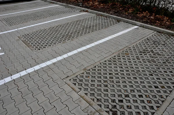new infiltration parking lot made of porous concrete tiles in a regular square grid with holes filled with gravel. in connection with the asphalt road and the sidewalk with interlocking paving