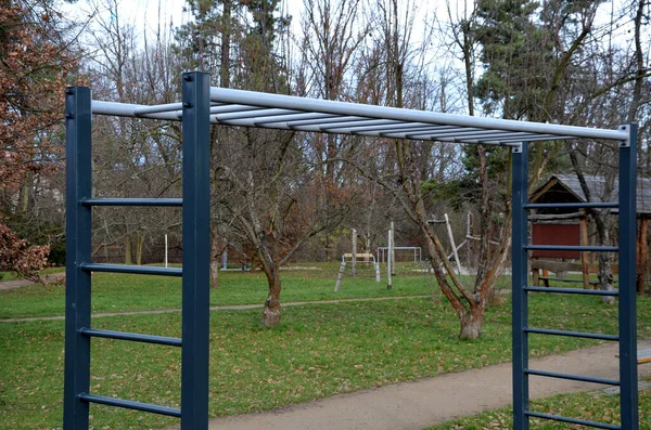 outdoor sports field. exercise equipment with gymnastic rings to strengthen the arms. bench for training the abdominal and back tendons and attachments, gray, steel, ladder