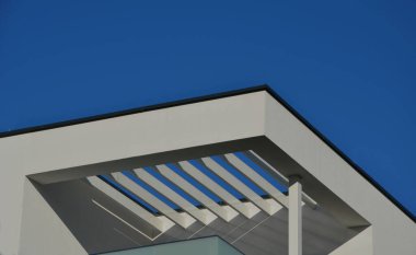 white square pergola with beams in white color are part of building on the upper floor. light is transmitted by trellises in stripes, glass railings, a white building with a flat roof in functionalist