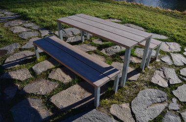 Stone slabs in the lawn, floor in the lawn shape of the rectangle camp site with a table and a urban bench, a lake. large flat blocks, picnic, fireplace, barbecue, park, boulder. sunny day