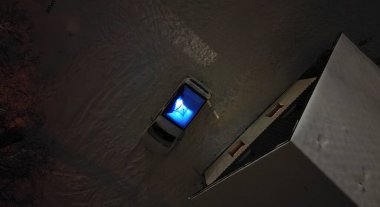 tourist in outdoor clothes will sleep in a blue tent directly on snow. support equipment for nature, experience an adventure in wilderness not far from cottage. lights up with a flashlight inside.