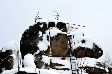 rocky outcrops with a view of the landscape. natural boulder rock completely covered with snow. climbing a frozen metal ladder. handrails made of simple pipes. built by a mountain tourist association