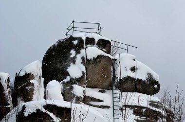 rocky outcrops with a view of the landscape. natural boulder rock completely covered with snow. climbing a frozen metal ladder. handrails made of simple pipes. built by a mountain tourist association