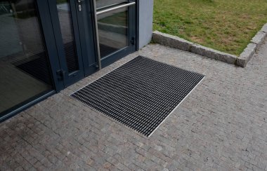 industrial mat cleaning zones at the entrance to the building. A black plastic-metal mat in the shape of an arch or half-circle lies on the limestone mosaic tiles, granite, cube, cobblestone, office