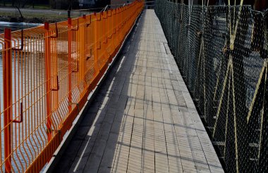 alternative pedestrian route over the bridge under repair. scaffolding and access ramps will guide people through the construction site above the river. orange mesh as a railing over the water