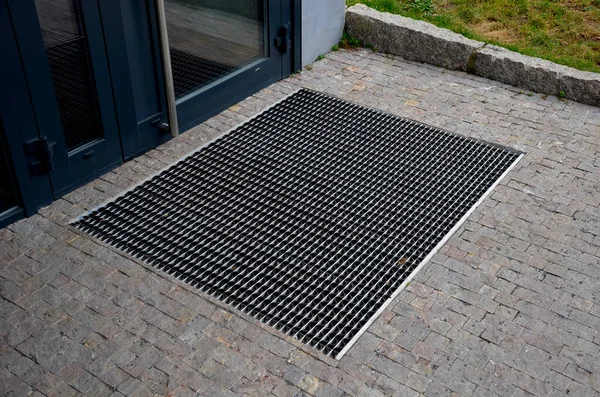 stock image industrial mat cleaning zones at the entrance to the building. A black plastic-metal mat in the shape of an arch or half-circle lies on the limestone mosaic tiles, granite, cube, cobblestone, office