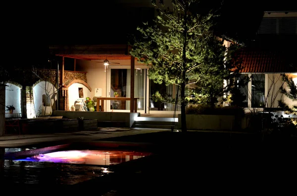 stock image backlit swimming pool frozen in ice in winter. an ideal bath after a sauna ritual. illuminated outdoor walls at night, a greenhouse with a pine tree and a terrace with a pergola, spotlight, brick arch