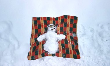 Bir kardan adam sırtüstü uzanmış bir şekilde bir battaniyeye uzanmış güneşleniyor. Güneş gözlüğü ve purosu var. Plajda tatil ya da kış kayak merkezinde. Dağdan İHA 'ya, İgloo' ya uç