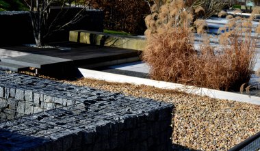 Süslü otlarla birlikte kırmızı ve yeşil kayın çiti. Baharın başında koyu kırmızı yapraklı yemyeşil alternatifler. Dağdan ve parkın yanından manzara, gabion, taş, duvar