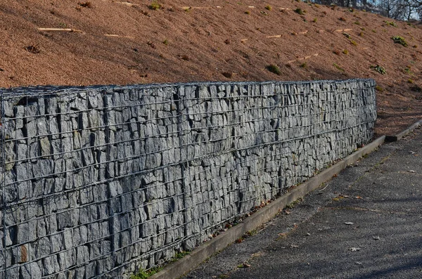 construction of a gabion retaining wall, as part of the house fencing. workers put geotextiles and on it wire baskets which consists of granite stones. demanding manual work
