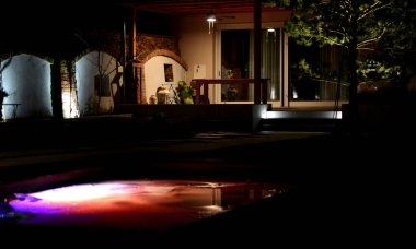 backlit swimming pool frozen in ice in winter. an ideal bath after a sauna ritual. illuminated outdoor walls at night, a greenhouse with a pine tree and a terrace with a pergola, spotlight, brick arch