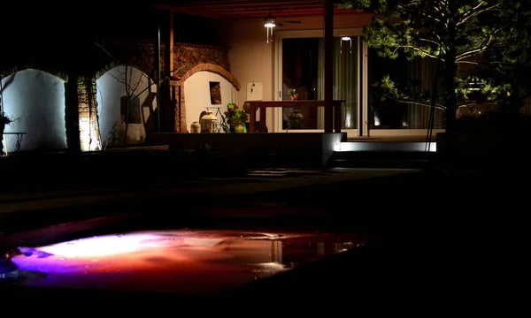 stock image backlit swimming pool frozen in ice in winter. an ideal bath after a sauna ritual. illuminated outdoor walls at night, a greenhouse with a pine tree and a terrace with a pergola, spotlight, brick arch