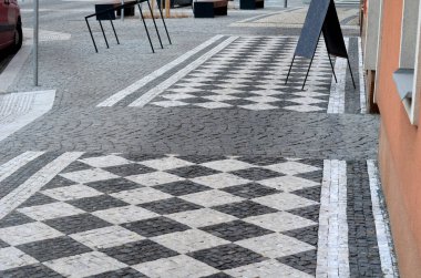 Çizgili beyaz mozaik mermer. Etrafında Gabion sepetlerinden duvarlar olan gri çizgili kaldırım. Gri metal bahçe kapısı. Çocuklar için düşük eskrim, satranç tahtası, desen, köşegen