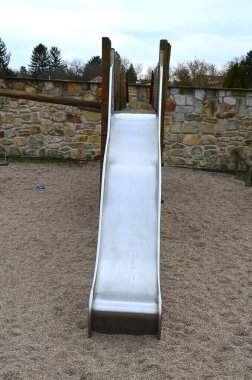 Kum havuzunda sürünen ahşap cazibe. Çocuklar paslanmaz çelik kaydırağına ve tırmanmak için halat ağına ve köprüde daha fazla güvenliğe sahipler. Anaokulunun arka planında kumtaşı duvar var.