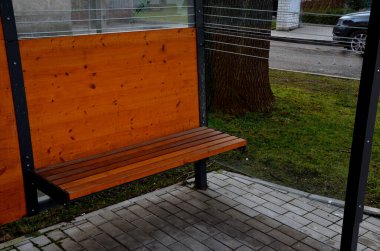 Şehir otobüs durağı. Entegre ahşap banklı cam bir sığınak. Sadece çatı ve arka duvar. Şehrin kaldırımının yanındaki caddede. Zarif kemer, istasyon, platform, çim, çatı, siyah, çerçeve, koltuk