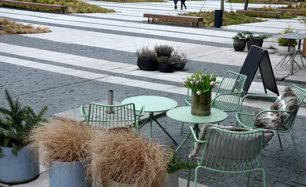 stock image Park furniture chess table and chairs for four persons made of light metal and wooden beams with backreston bright glade area gravel lawn green beige gray evening sun spring