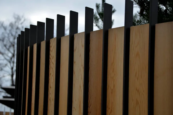 luxurious fencing in a combination of black metal rods made of grass vertically folded into an arch. the wood is between the metal bars and forms a solid opaque wall. the garden has privacy