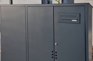 Beyaz bir duvardaki paslanmaz çelik bir posta kutusuna uzanan bir adam elini bir deliğe atar ya da içeriden bir şey azarlar.