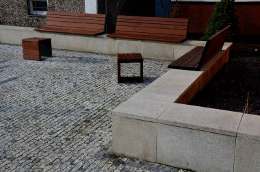 Meydandaki ağacın altındaki kaldırımda kirli, soğuk sallanan sandalye. Parktaki tek bir kişi için tropikal ahşaptan yapılmış ahşap sandalyeler. Kar, küp, kahverengi tahtalardan yapılmış rahat çelik çerçeveler, çam