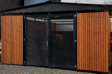 Ahşap panelli ve şeffaf ağ kapılı bir garaj. Pansiyonun yanındaki çöp deposunda. Sığınaktaki vatandaşların mal varlığını ve düzenini koruyor. Araba güvenli ve karsız, kaldırım taşı