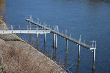 Kanalın koruyucu yapısı. Kütükleri ve buzu kenara itiyor. Yüzen iskele su seviyesindeki dalgalanmalara tepki veriyor. Hidroelektrik santralin altına demir atmış.