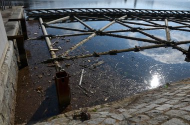 Kanalın koruyucu yapısı. Kütükleri ve buzu kenara itiyor. Yüzen iskele su seviyesindeki dalgalanmalara tepki veriyor. Hidroelektrik santralin altına demir atmış.