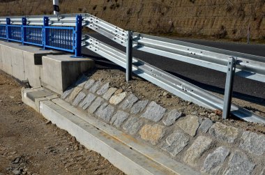 Yolun kenarında beton bir duvarla güçlendirilmiş yol bariyerleri ve mavi parmaklıklar var. Otobanın yüzeyinden süzülen yağmur suları için oluklar. güçlendirilmiş beton