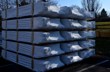 Yığınla ürünün olduğu bir depo. Yüksek raflarda depolanmış ve beyaz folyoya sarılmış. Ahşap ürünün sudan ve yağmurdan korunması.