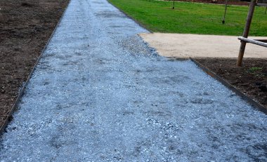 Kum tekeri. Bahçe el arabası bir işçi taşır ve park, orman ve toprak yolu onarmak için bej çakıl yığınlarının üzerine dökülür. Erozyon, yenilenmesi gereken çakılları alıp götürür.