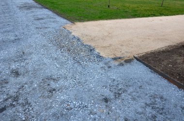 Kum tekeri. Bahçe el arabası bir işçi taşır ve park, orman ve toprak yolu onarmak için bej çakıl yığınlarının üzerine dökülür. Erozyon, yenilenmesi gereken çakılları alıp götürür.