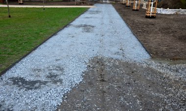 Kum tekeri. Bahçe el arabası bir işçi taşır ve park, orman ve toprak yolu onarmak için bej çakıl yığınlarının üzerine dökülür. Erozyon, yenilenmesi gereken çakılları alıp götürür.