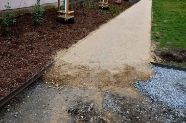 Kum tekeri. Bahçe el arabası bir işçi taşır ve park, orman ve toprak yolu onarmak için bej çakıl yığınlarının üzerine dökülür. Erozyon, yenilenmesi gereken çakılları alıp götürür.