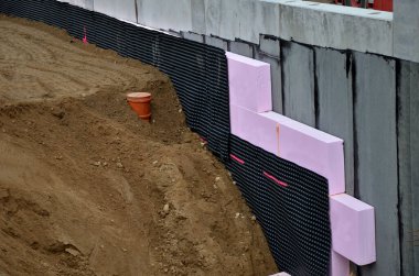 Yeraltı katının çevresinde polistiren plakalar olan termal yalıtım. Kaynamış folyoyla suya ve neme karşı izolasyon. Binanın etrafını doldur. Toprak serpme temeli