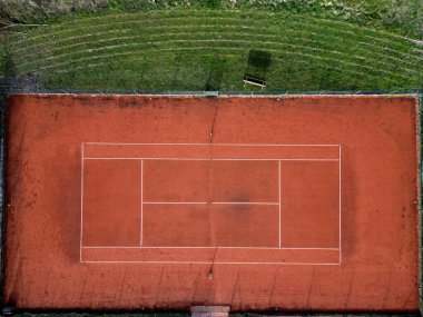 Kırık tuğlalardan oluşan kırmızı bir yüzeyi olan tenis kortu. Oyun alanındaki kilin düzenli bakıma ihtiyacı var. Oyundan önce yuvarlanan ve süpüren tozlu yüzeylere su serpilmeli.