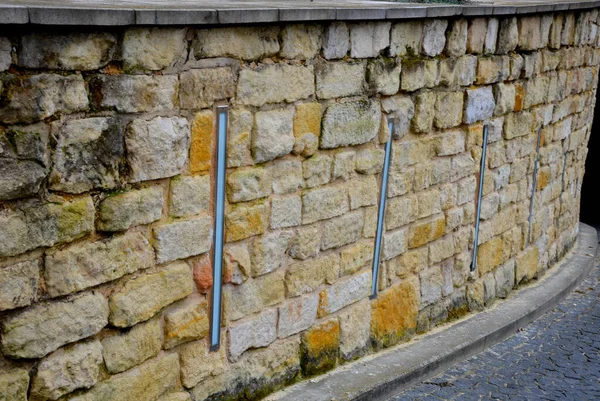 beautifully folded retaining wall with granite attic with small joints. brown beige yellow irregular gneiss holding slope above it. long vertically placed lights inside the wall. entrance to garage