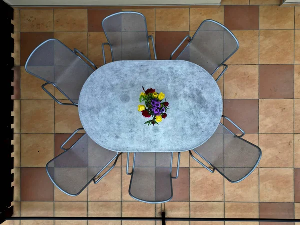 花瓶に美しい花が配置された家のテラス タイルの茶色と黄色の舗装 楕円形のテーブルと金属グレーの椅子 金属製の手すりドローンビュー 花壇が芝生を取り囲み — ストック写真