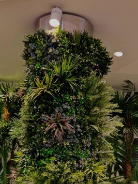 Otel lobisindeki yeşil bitki örtüsü sütunları, ofisler. Işık halojenleri fotosentez yapmak için bitkilerin üzerinde parlıyor. Sulama pompaları ve hortumların karmaşık sistemi plastik çiçeklerle değiştirilebilir