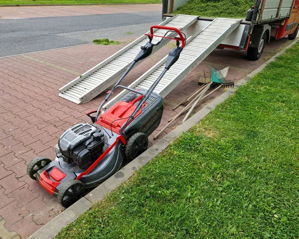 a truck loaded with cut grass. ramps for large mowers made of aluminum profiles. a lawnmower is waiting ready to work in the parking lot of a shopping center. red
